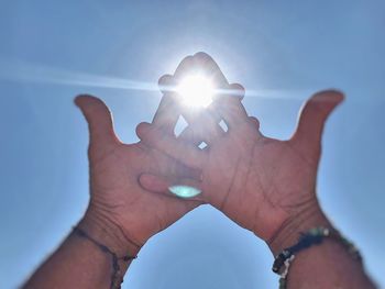 Midsection of person holding sun shining over blue sky