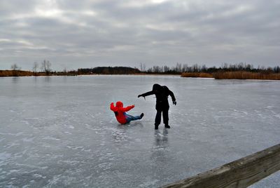 People on lake against sky during winter