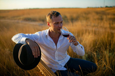 Young man drinks wine in wild field