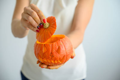 Cropped image of woman holding pumpkin against orange background