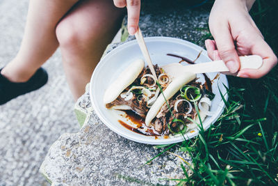 Low section of person sitting on retaining wall with food plate