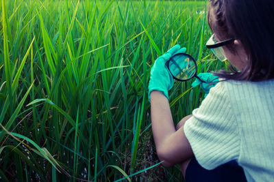 Woman looking at grass through magnifying glass on field