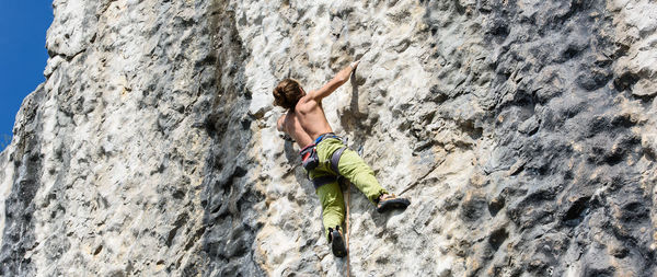 Low angle view of shirtless man climbing on rock