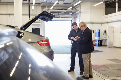 Customer and mechanic using mobile app while standing by car in repair shop