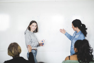 Mature teacher assisting teenage student while standing by whiteboard in classroom