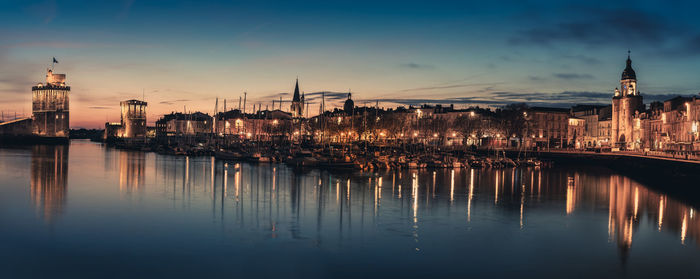 Scenic view of river by illuminated buildings against sky during sunset