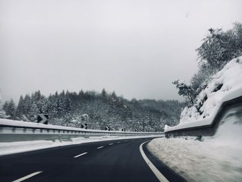 Snow covered road by trees against clear sky