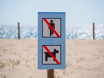 Close-up of warning sign on beach against sky