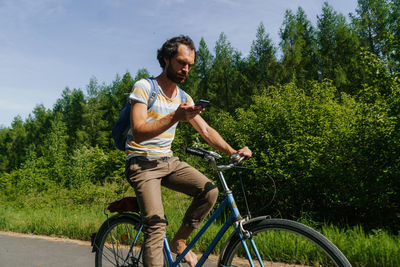 Man using mobile phone while riding bicycle by grassy field