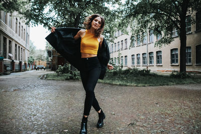 Full length portrait of young woman standing on walkway in city