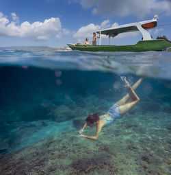 Young woman snorkeling near the boat in ocean, underwater view