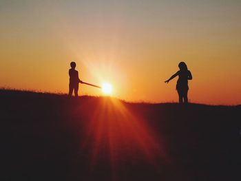 Silhouette man standing on field against orange sky
