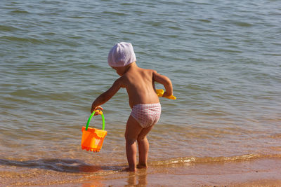 Rear view of shirtless boy standing in sea