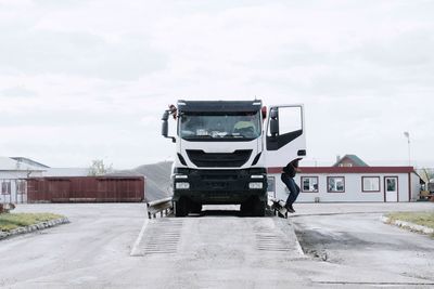 Side view of man by truck on road against cloudy sky