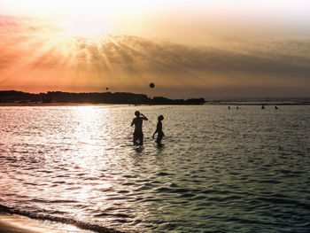 Silhouette people on sea against sky during sunset