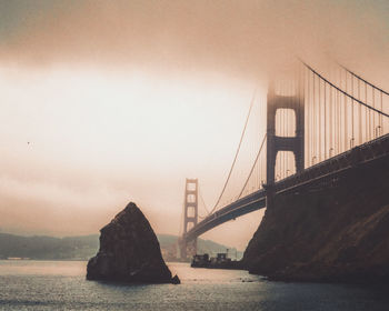 Suspension bridge over sea against sky during foggy weather