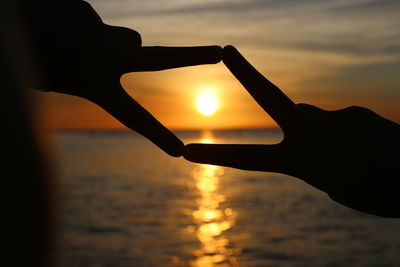 Close-up of silhouette hand against sea during sunset