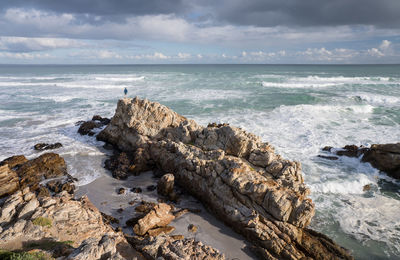 Rock formations by sea against cloudy sky