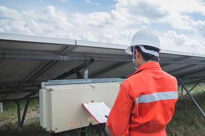 Side view of worker talking on phone while standing by solar panel