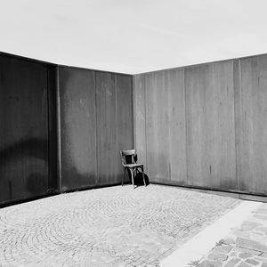 Empty chair against wall on building terrace during sunny day