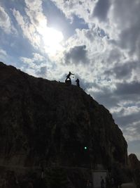 Low angle view of silhouette man on cliff against sky