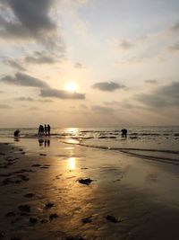 Silhouette people on beach against sky during sunset