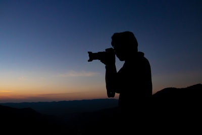 Silhouette man photographing at camera against sky during sunset