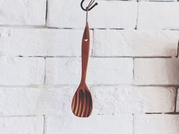 Close-up of wooden spoon hanging against white wall