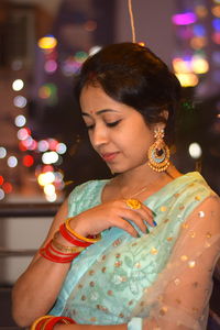 Beautiful woman wearing sari standing against illuminated lighting