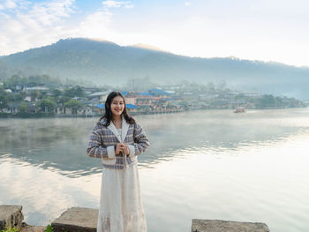 Happy asian woman standing at lakeside with fog on the lake view in morning at ban rak thai village
