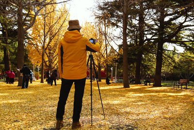 Rear view of man photographing while standing in park during autumn