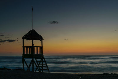 Lifeguard hut on beach against sky during sunset