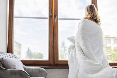 Rear view of woman sitting on bed at home