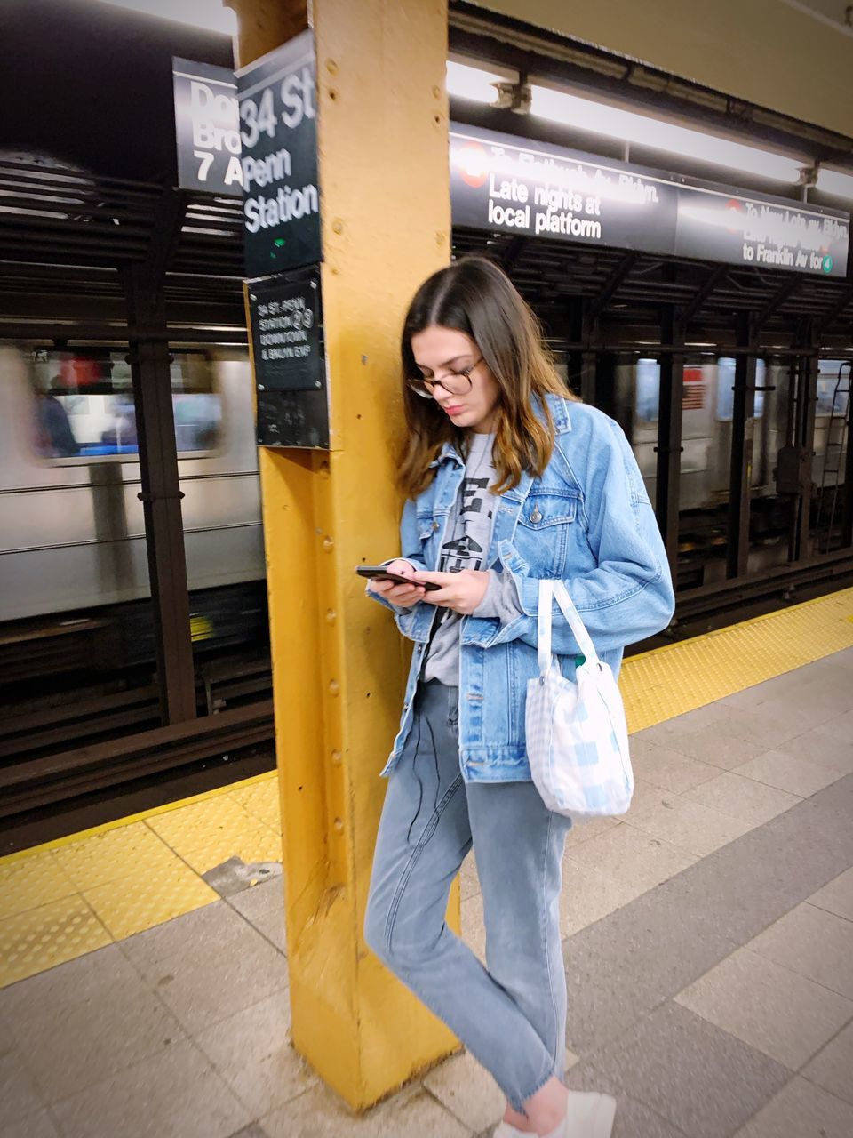 one person, communication, casual clothing, public transportation, technology, women, lifestyles, standing, real people, railroad station platform, railroad station, young adult, rail transportation, young women, wireless technology, transportation, mobile phone, holding, adult, beautiful woman, hairstyle, subway train