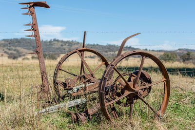 Old rusty wheel on field against sky