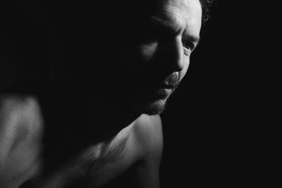 Close-up portrait of shirtless man against black background