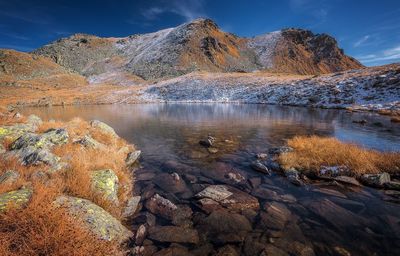 Rocks in lake by mountains against sky