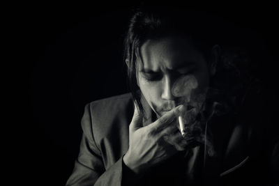 Portrait of young man smoking cigarette against black background