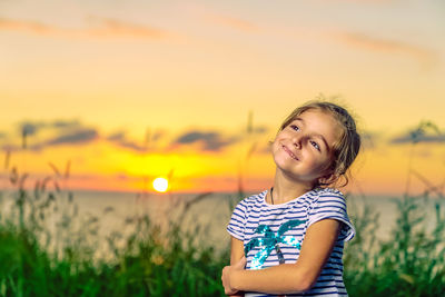 Portrait of smiling girl standing on field against sky during sunset