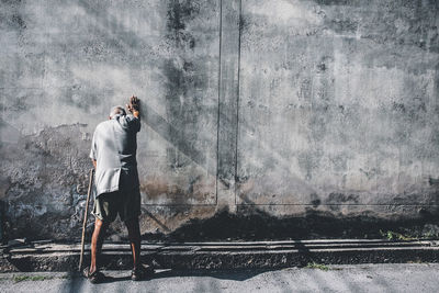 Full length rear view of senior man standing against wall