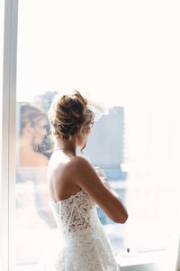 Close-up of woman with arms outstretched standing against window