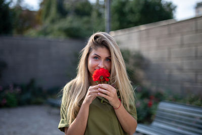 Portrait of woman smelling red flower in city