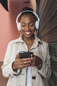 Happy woman wearing headphones text messaging through mobile phone while listening music by shutter