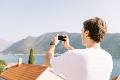 Side view of man photographing against sky