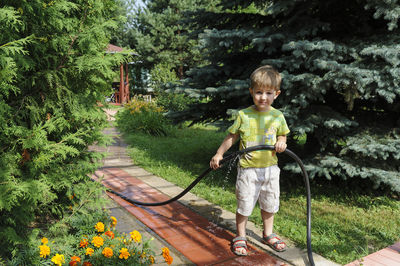 Full length portrait of smiling boy holding garden hose while standing in lawn