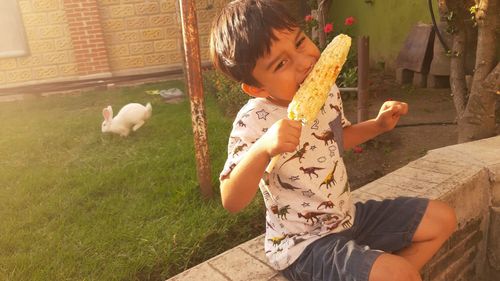 Cute boy eating corn while sitting on retaining wall