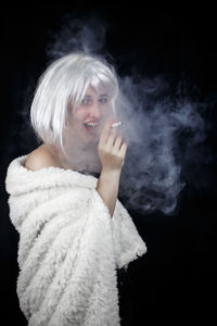 Portrait of female model smoking cigarette against black background