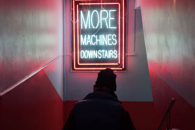 Rear view of man standing against illuminated wall