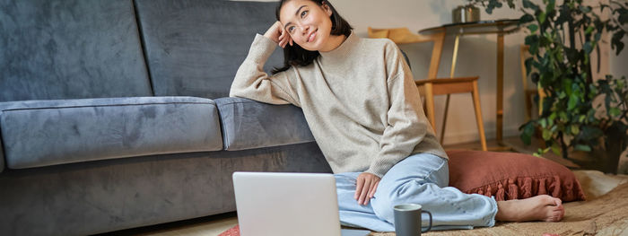 Young woman using digital tablet while sitting on sofa at home