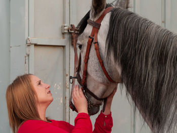 Young woman touching horse while standing against metal built structure